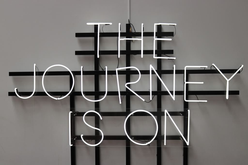 Black and white image of a neon sign reading "The Journey Is On" 
Source: Unsplash