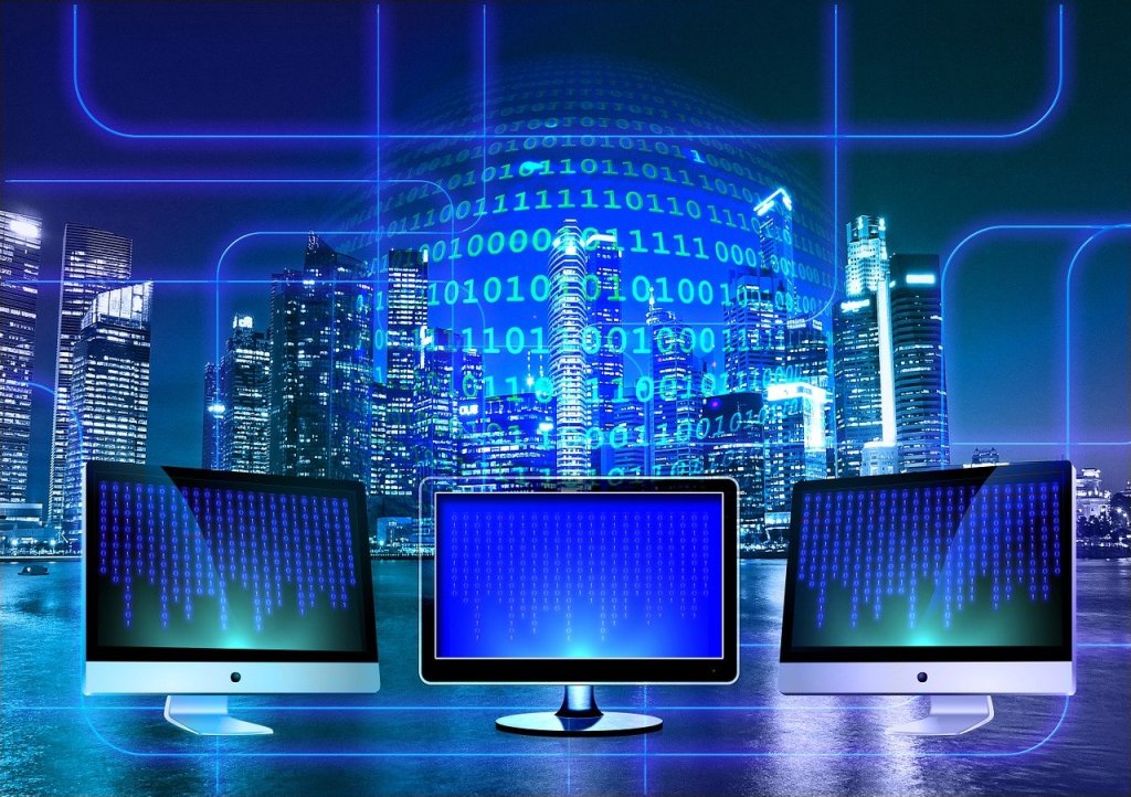 Image of three monitors behind which are binary code with a city skyline. 
Image sourced via Pixabay.