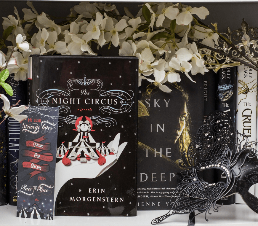 Photo of The Night Circus by Erin Morgenstern with Sky in the Deep by Adrienne Young with a bookmark, black mask and white flowers.
(c) Aimee Davis @writingwaimee on Instagram.