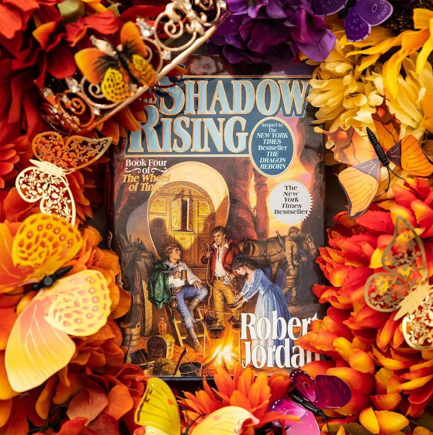 Photo of the book The Shadow Rising from the Wheel of Time series by  Robert Jordan surrounded by orange flowers and orange and gold butterflies. 
(c) Aimee Davis @writingwaimee on Instagram