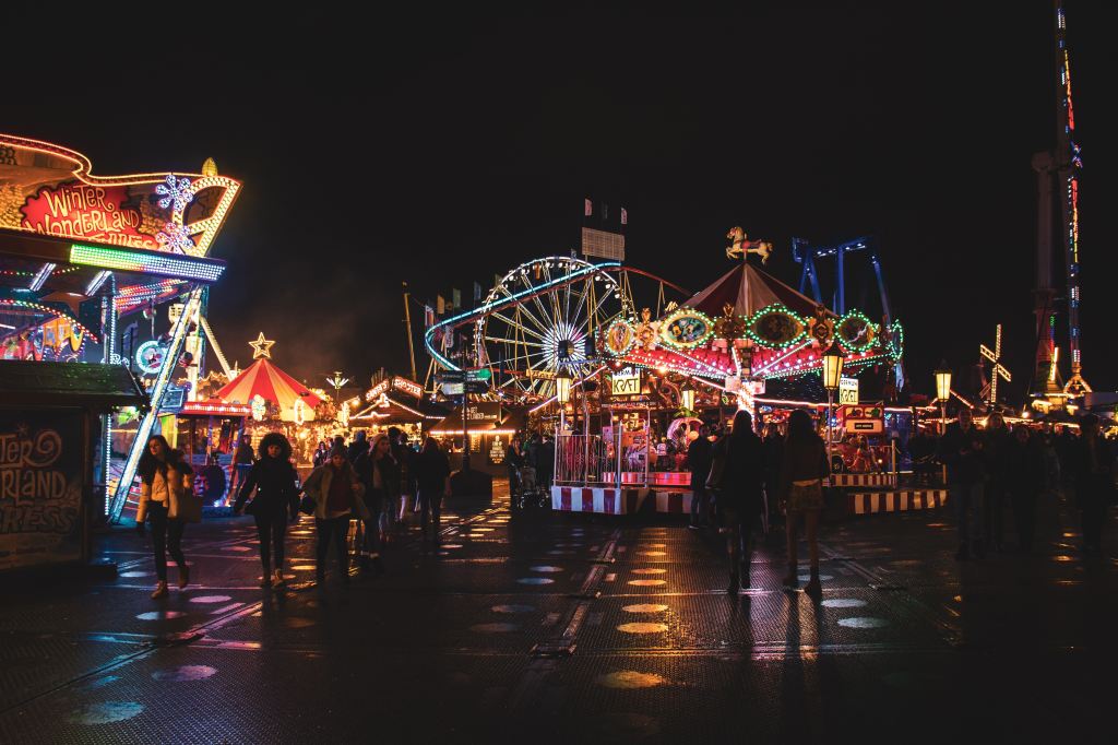 Photo of a county fair at night with rides in lights, carousel and roller coaster in the background. 