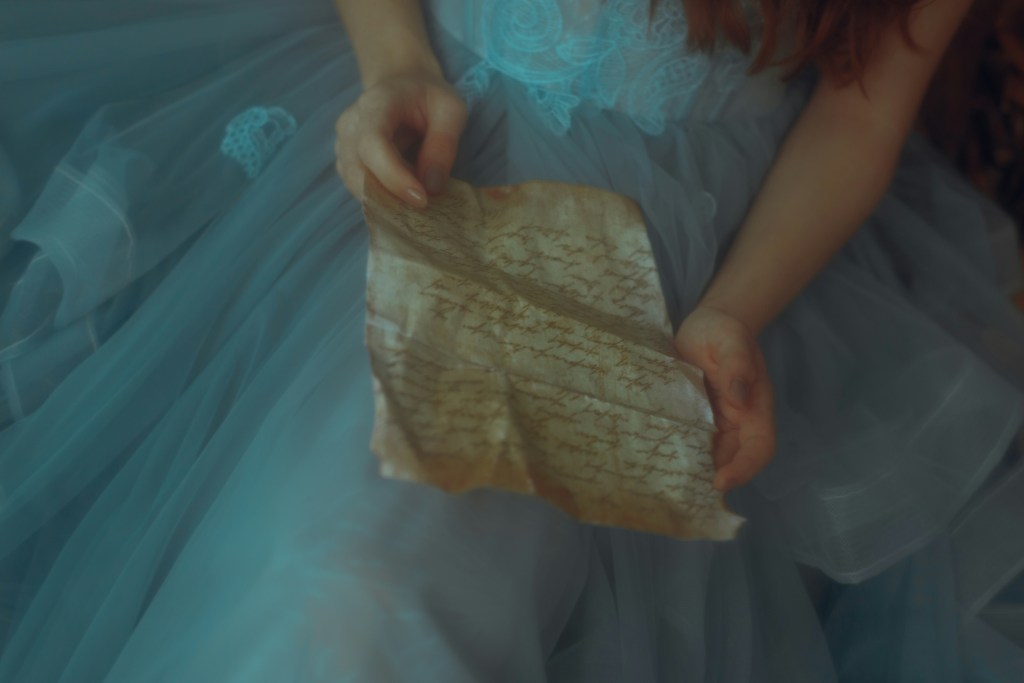 Image of the torso of a girl in a blue ruffled gown reading a piece of parchment. 
Photo by SAMANTA SANTY on Unsplash